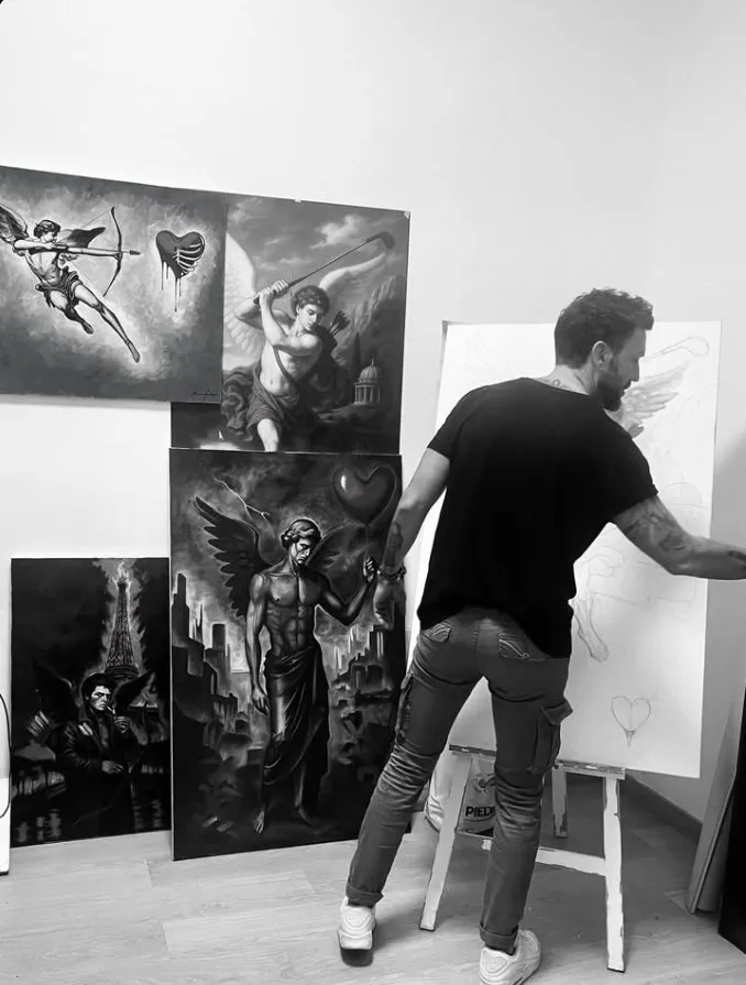 Fernando Sanz pintando en su estudio, rodeado de varios de sus lienzos de ángeles y cupidos (fotografía en blanco y negro)
