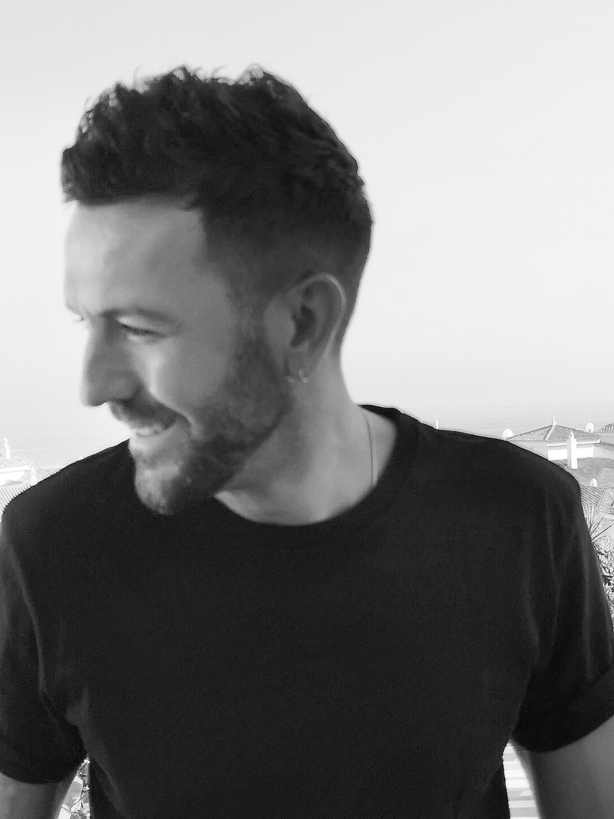Retrato en blanco y negro de Fernando Sanz, sonriendo y mirando hacia un lado, con camiseta negra